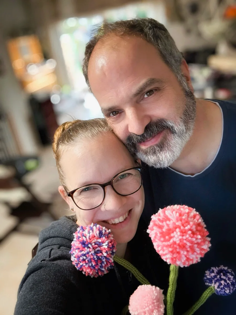 Zwei lächelnde Menschen mit bunten Wollblumen als persönliches Stimmungsbild der Wollsymphonie.